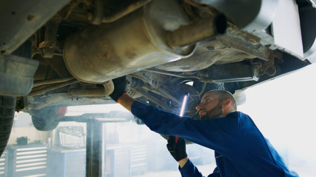 Qualifizierter Mechaniker führt in einer professionellen Werkstatt gründliche Wartungsarbeiten an Fahrzeugen von unten durch.